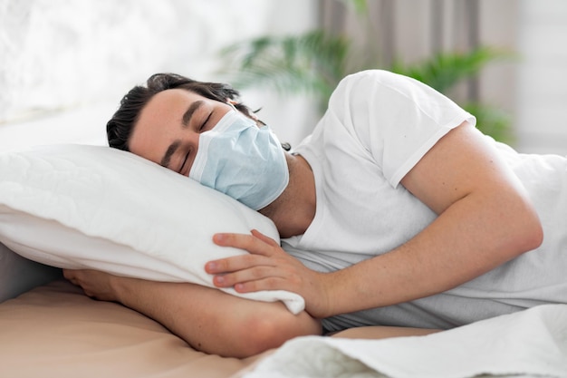 Kranker Mann in medizinischer Maske, der im Bett an Virus leidet