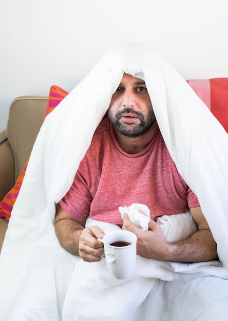 Kranker Mann mit Grippe und Coronavirus, bedeckt mit der Decke.