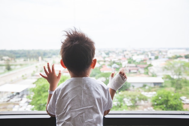 Krankes asiatisches Kind im Krankenhaus, das durch das Fenster nach draußen schaut