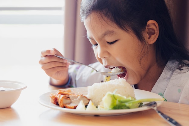 Krankes asiatisches Mädchen, das gesundes Essen zum Mittagessen isst, während es in privaten Patientenzimmern im Krankenhaus bleibt. Gesundheits- und Lifestyle-Konzept.