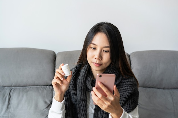 Krankes asiatisches Mädchen, das zu Hause auf dem Sofa im Wohnzimmer sitzt, und Videokonferenz-Online-Live-Gespräch aus der Ferne mit Arzt für Gesundheitsberatung, freier Platz. Telemedizin, Heimisolationskonzept.