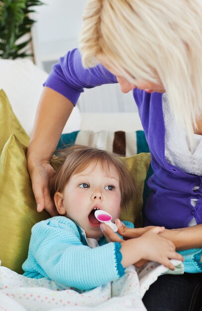 Krankes kleines Mädchen, das Sirup von ihrer mitfühlenden Mutter erhält