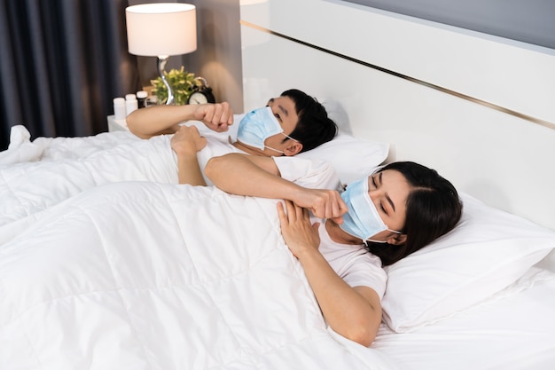 Krankes Paar in der medizinischen Maske, die hustet und an Viruskrankheit und Fieber im Bett leidet, Coronavirus-Pandemiekonzept.