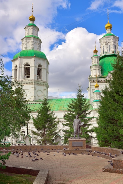 Krasnoyarsk, Sibéria, Rússia-09.01.2021: Estátua do artista russo "Surikov Vasily Ivanovich" no contexto da igreja mais antiga do século XVIII no estilo barroco da Sibéria