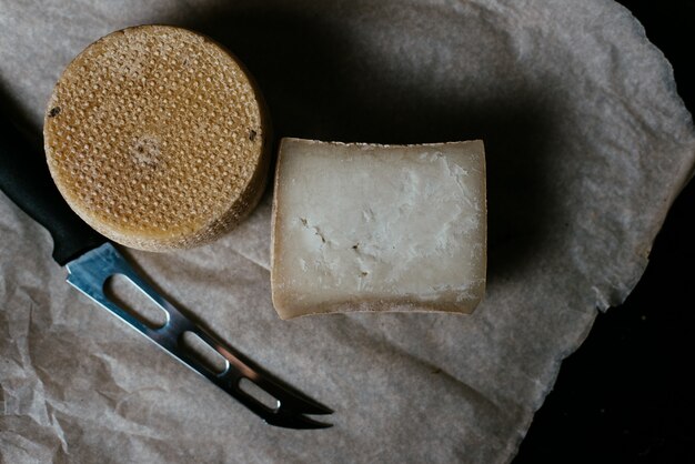 Kravot de queso duro o parmesano en un tablero oscuro de madera. Cuchillo de queso al lado de las cabezas de queso