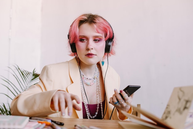kreative junge Frau mit Smartphone hört Musik am Tisch mit Skizzenbuch und Malmarkierern