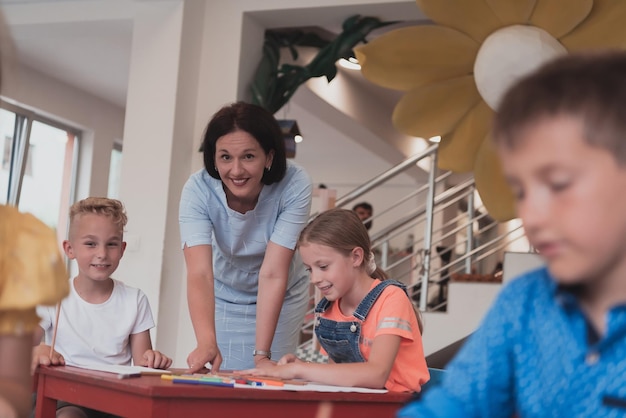 Kreative Kinder während eines Kunstunterrichts in einer Kindertagesstätte oder im Klassenzimmer der Grundschule, die mit einer Lehrerin zeichnet