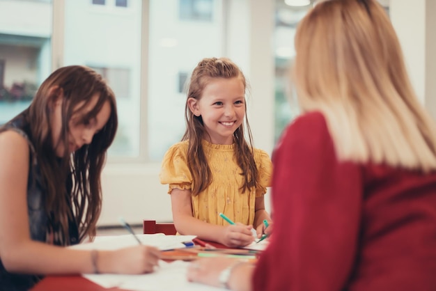 Kreative Kinder während eines Kunstunterrichts in einer Kindertagesstätte oder im Klassenzimmer der Grundschule, die mit einer Lehrerin zeichnet