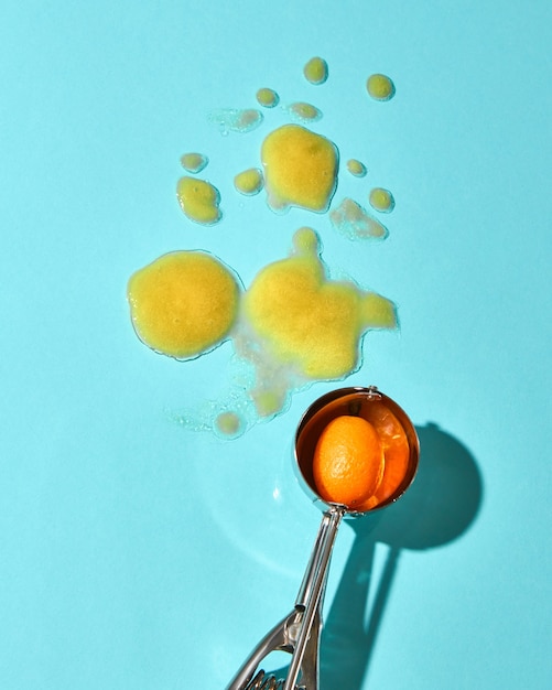 Kreative Komposition aus einer Kugel gelben Eises auf einem Metalllöffel auf einem blauen Glashintergrund mit Schatten. Essen im modernen Stil.