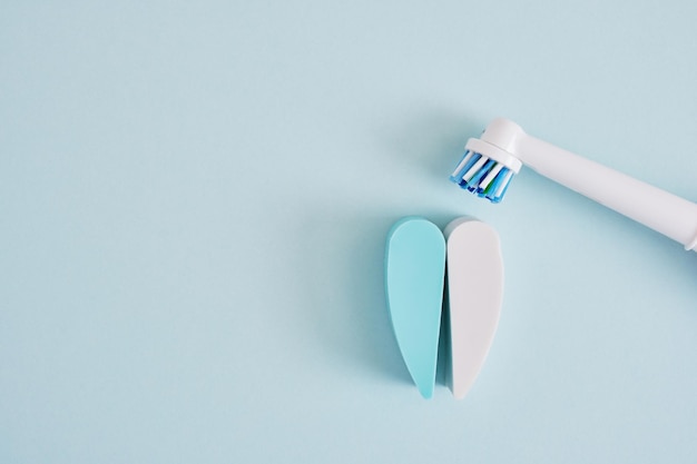 Kreative Komposition aus elektrischer Zahnbürste und Zähnen auf blauem Hintergrund, deren Bürsten effektiver bei der Reinigung der Mundhöhle und umweltfreundlicher sind
