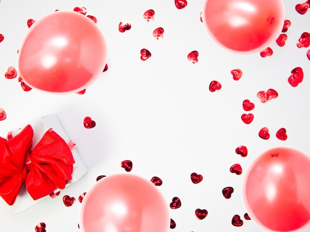 Kreative Komposition aus Herzen und weißer Geschenkbox mit rotem Band und Luftballons auf weißem Hintergrund mit Kopienraum, glücklicher Valentinstag, Muttertag, flache Lage, Draufsicht