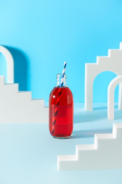 Kreative Komposition mit Cranberry-Limonaden-Cocktail in Flasche auf blauem Hintergrund