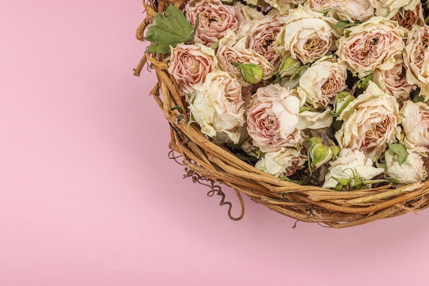 Kreative Komposition mit trockenen, zarten Rosen in einem hausgemachten Gitterkorb Grußkarte mit pastellrosafem Hintergrund