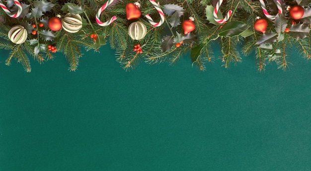 Kreative Weihnachtswohnung lag auf grünem Papier mit roten Verzierungen, viel Platz zum Kopieren. Natürliche Tannen- und Stechpalmenzweige, verziert mit Zuckerstangen, Glasschmuck und trockenen Limettenfrüchten.