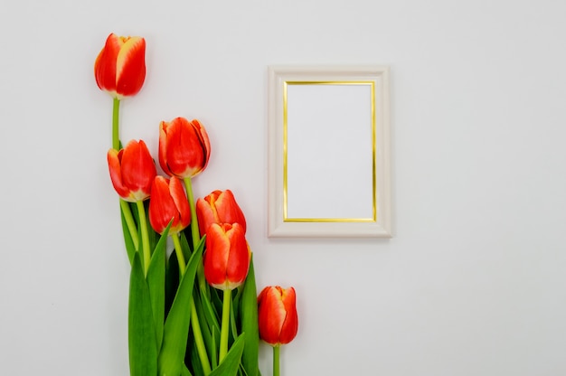 Kreative Zusammensetzung mit Fotorahmenmodell, rote Tulpen auf abstraktem Hintergrund.