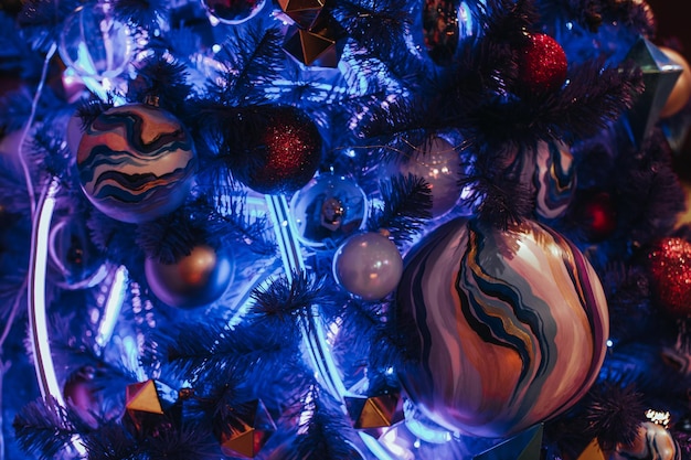 Kreativer blauer Weihnachtsbaum geschmückt mit handgemalter Weihnachtskugel und Neongirlande Magic