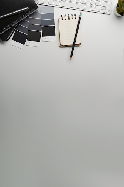 Kreativer Designer-Arbeitsplatz mit Notizbuch, Farbfeldern, Tastatur und Kopienraum auf weißem Hintergrund