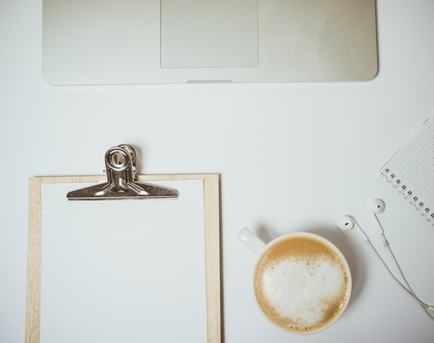 Kreativer Desktop mit Laptop-Kaffee und Schreibwaren auf weißem Tisch Draufsicht Flache Lage