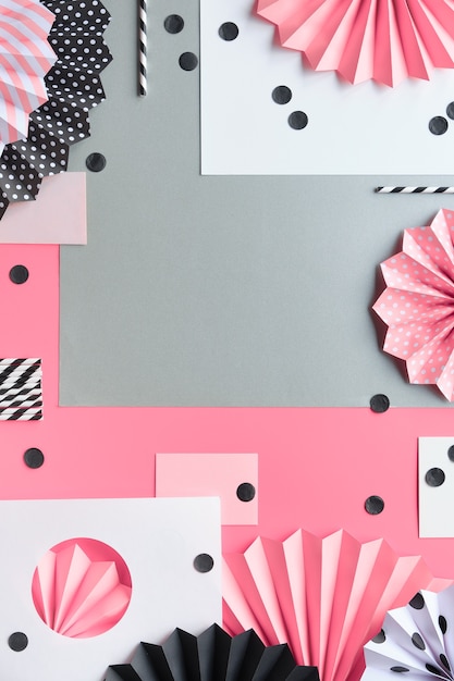 Kreativer Hintergrund auf geschichtetem Papier. Gefaltete Papierfächer und Konfetti auf Schwarz, Pink und Weiß.