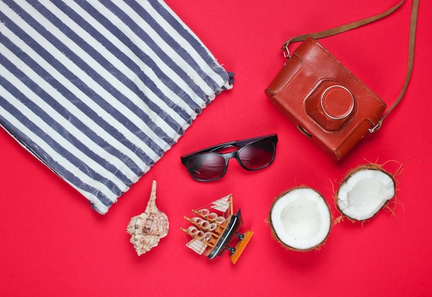 Kreativer Hintergrund des Sommers. Strand gestreifte Tasche, Zubehör auf rotem Hintergrund. Draufsicht.