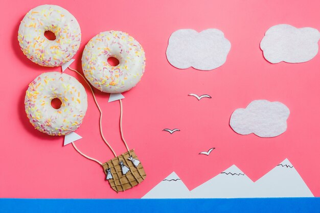 Kreativer Lebensmittel-Minimalismus, Donut in Form des Luftfahrzeugs im rosa Himmel mit Wolken, Berge, Draufsicht, Kopien-Raum, Reise