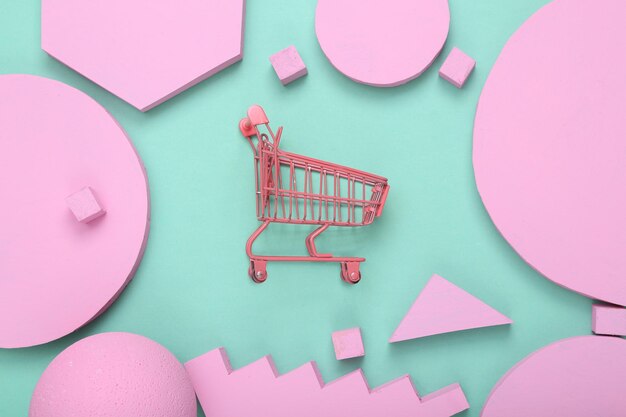 Kreatives Einkaufslayout Rosa Supermarktwagen mit rosa verschiedenen geometrischen Formen auf minzblauem Hintergrund Pastellfarben Trend Minimalismus Konzeptkunst Flache Ansicht von oben