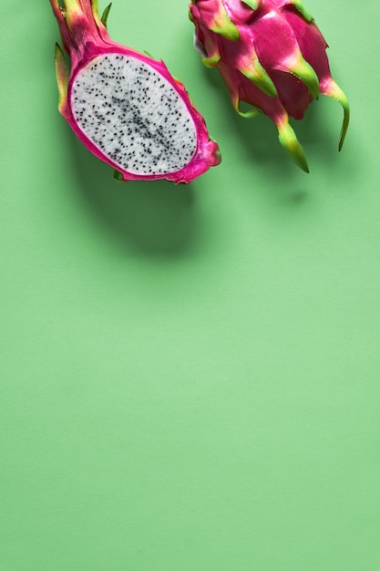Kreatives flaches Layout mit frischen organischen rosa, weißen und grünen Drachenfrüchten (Pitaya oder Pitahaya) auf lebendigem grünem Minzpapierhintergrund. Trendige Draufsicht, Kopierraum. Flache Fruchtlage halbiert.