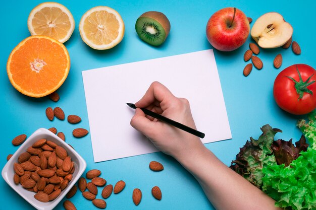 Kreatives Layout aus verschiedenem Obst, Gemüse und Nüssen mit weißem Papierblatt Freier Speicherplatz