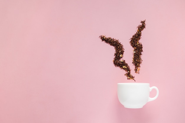 Kreatives Layout der weißen Tasse mit trockenen Blumen eines grünen Tees auf dem rosa Hintergrund