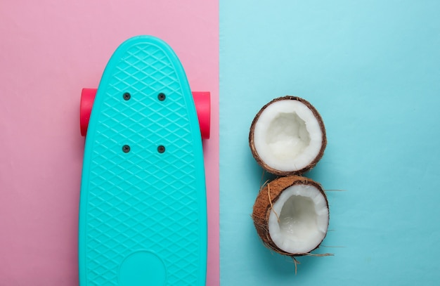 Kreatives sommerkonzept. skateboard, kokosnusshälften auf blauem rosa hintergrund. pastellfarbentrend.