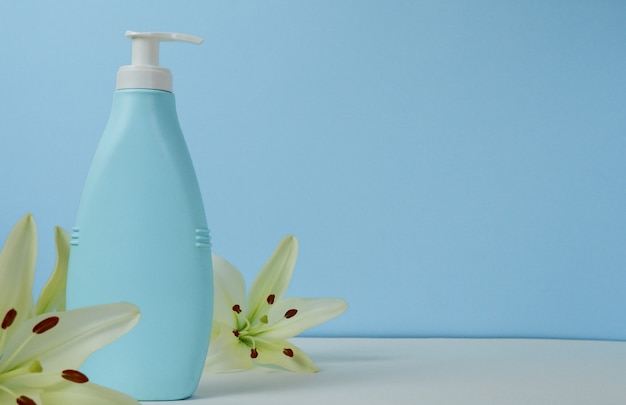 Kreatives Stillleben-Make-up-Foto mit blauer Kosmetikflasche mit Spender und frischen Lilienblumen