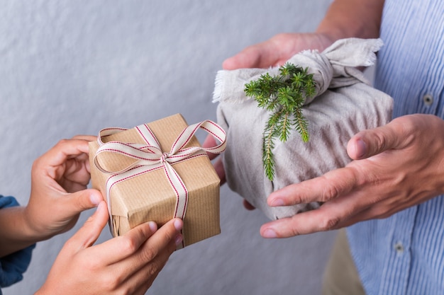 Kreatives Zero-Waste-Weihnachtskonzept. Menschen tauschen handgemachte Geschenkboxen aus, die in umweltfreundlichem Kraftpapier und traditionellem Furoshiki-Stoff im japanischen Stil verpackt sind. Familienzeit, festliche Vorbereitung.