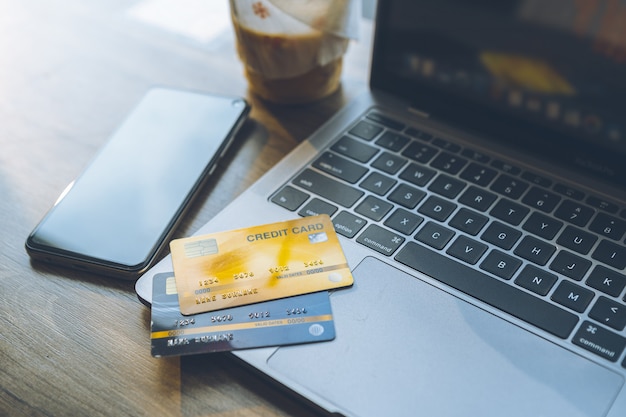 Kreditkarte von Laptop, Smartphone und Kaffeetasse auf Holzhintergrund, Online-Banking-Konzept