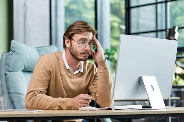 Kreditkartentransaktion fehlgeschlagen Ein verärgerter junger Mann sitzt im Büro am Tisch und schaut sich das an