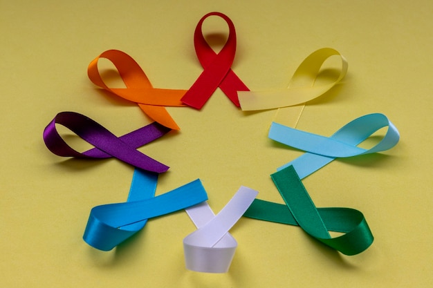 Kreis mit bunten Bändern von Krankheits- und Krebspräventionskampagnen mit gelbem Hintergrund.