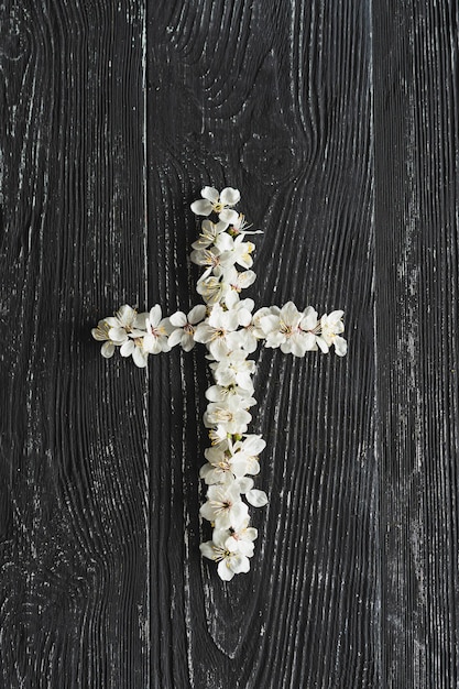 Kreuz, das den Tod und die Auferstehung Jesu Christi symbolisiert. Frühlingsblumen auf einem Holzhintergrund