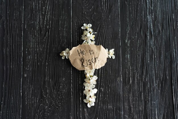 Foto kreuz mit blumen auf einem hölzernen hintergrund mit der inschrift christus ist auferstanden.