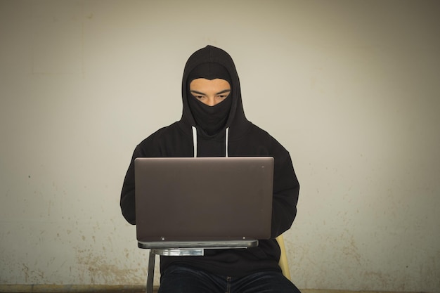 Krimineller benutzt Laptop, während er an der Wand sitzt