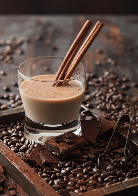 Kristallglas aus Irish Cream Baileys Likör mit Zimtkaffeebohnen und Pulver mit dunkler Schokolade in Holzschale auf dunklem Holzhintergrund Draufsicht