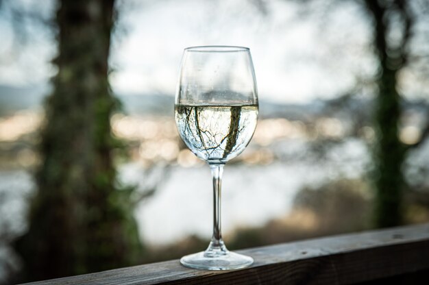 Kristallglas mit Weißwein auf Holzgeländer auf Terrasse des Hauses in der Natur platziert