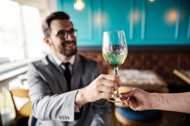 Kristallglas voller Weißwein Ein männlicher Gast im Business-Anzug sitzt an einem Tisch in einem Restaurant und nimmt ein Glas kalten Alkohol. Fokussieren Sie die Fotos auf die Hände, die ein Glas Wein halten