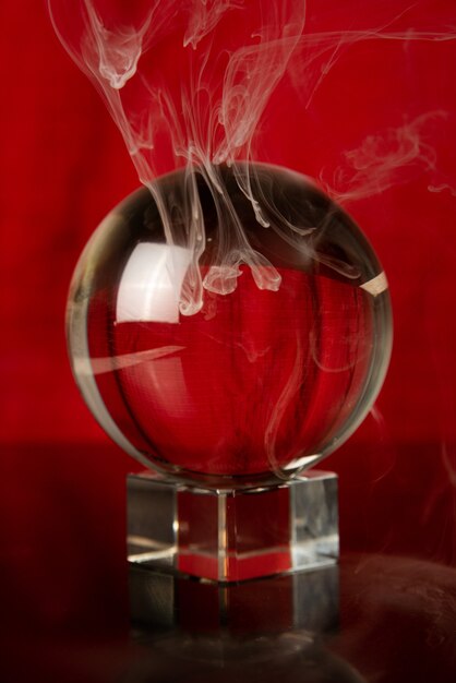 Kristallkugel mit rotem Hintergrund und fallendem Rauch, selektiver Fokus.