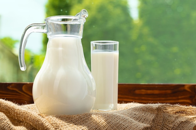 Krug Milch auf Holztisch gegen unscharfen Laubhintergrund schließen