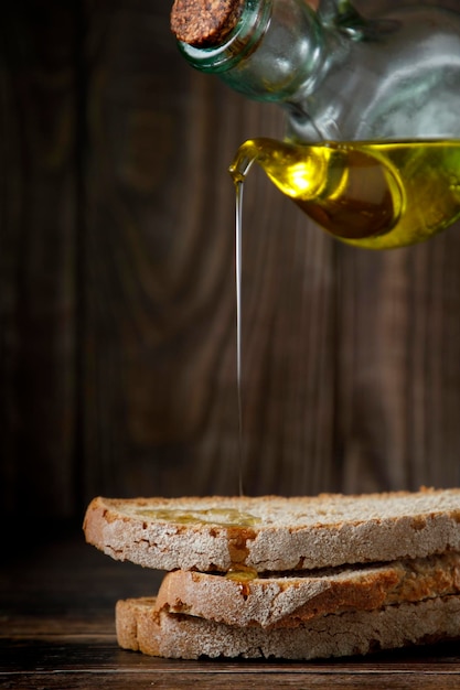 Krug Olivenöl tropft auf Scheiben Weißbrot