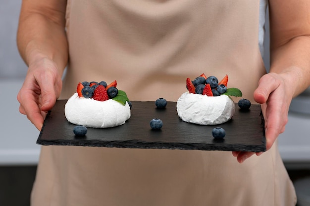 Kuchen Anna Pavlova auf schwarzem Tablett in den Händen des Konditors Meringue-Kuchen mit frischen Beeren