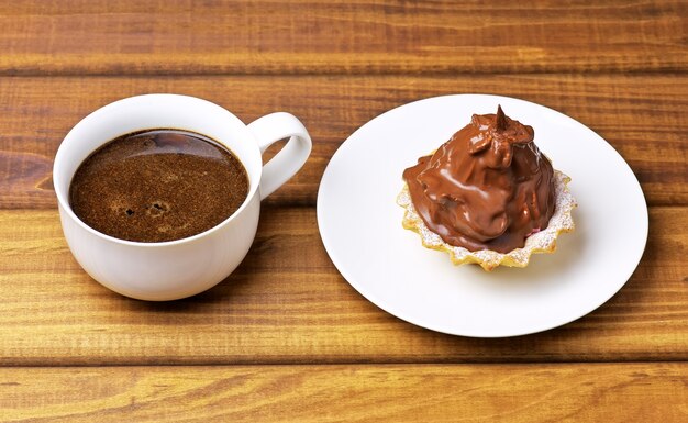 Kuchen auf einem Teller und eine Tasse Kaffee auf Holztisch