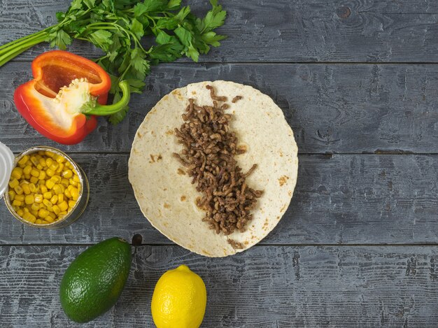 Kuchen aus Maismehl mit Rinderhackfleisch auf einem Holztisch und Zutaten für mexikanische Tacos