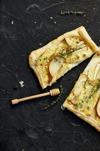 Kuchen gebacken in Blätterteig mit Gorgonzola-Käse und Birnen auf schwarzem Tisch