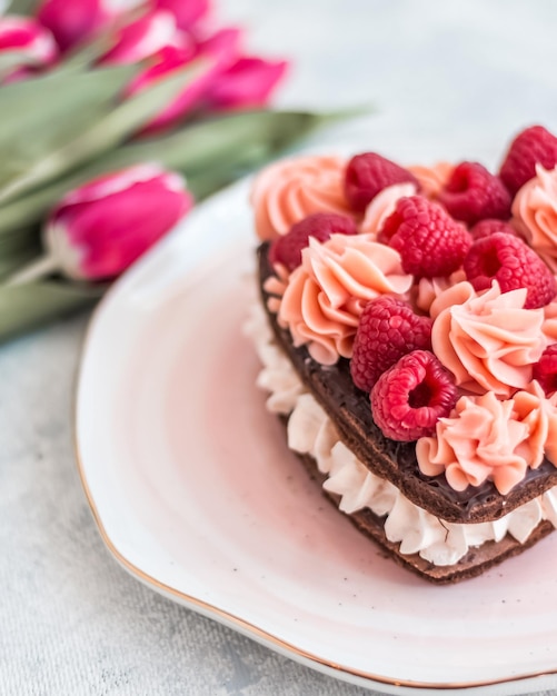 Kuchen in Form eines Herzens aus traditionellem französischen Dessert-Eclair und Pavlov-Keksen auf weißem Hintergrund mit Tulpen Valentinstag-Konzept