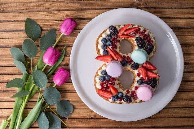 Kuchen in Form von Nummer 8, dekoriert mit Beeren und Blumentulpen